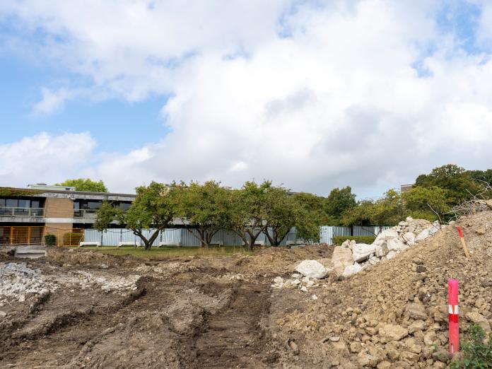 Byggeplads med grus og træer.